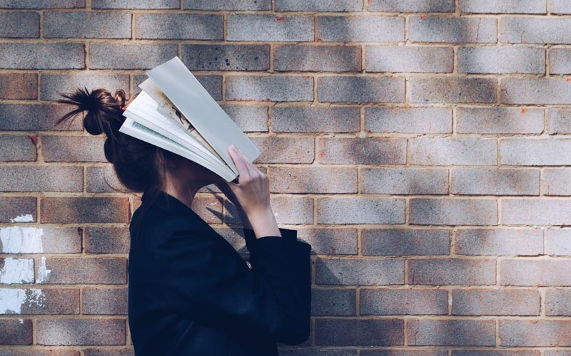teenage girl covering face with open book